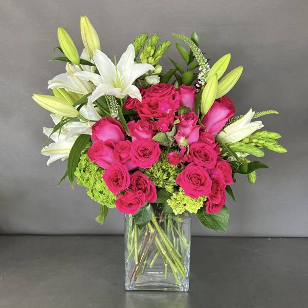 Pink roses and white lilies arranged in a clear square vase