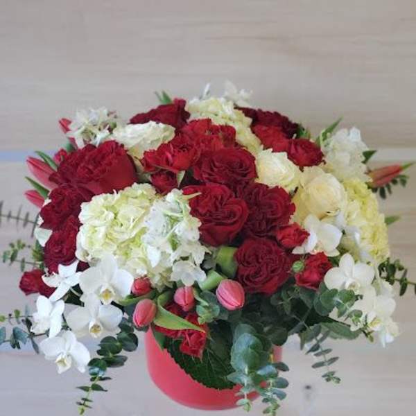 Round arrangement of red roses, white hydrangeas, orchids and pink tulips in a red hat box