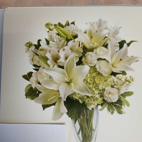 White lilies and mixed white flowers in a clear glass vase