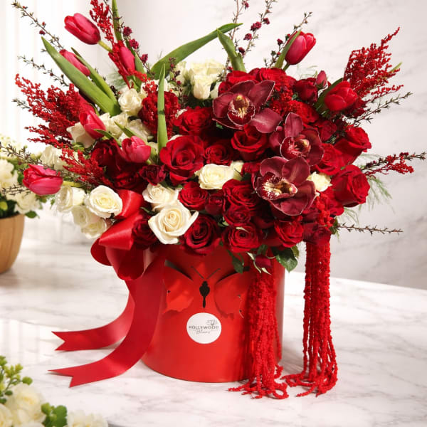 Red and white rose arrangement with tulips in a red hatbox
