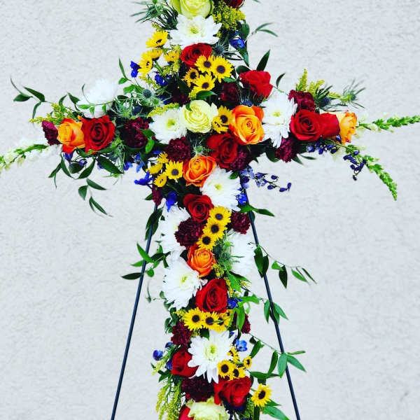 Cross-shaped floral tribute with red, orange, yellow, and white flowers