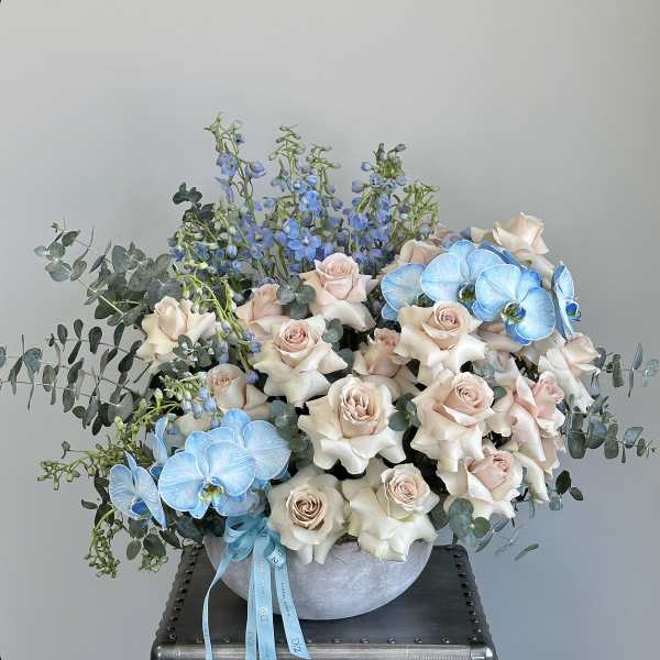 Cream roses and blue orchids in a round vase with eucalyptus