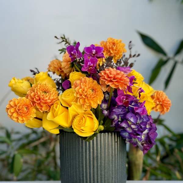 Bouquet of yellow roses, orange dahlias, and purple orchids in a ribbed vase