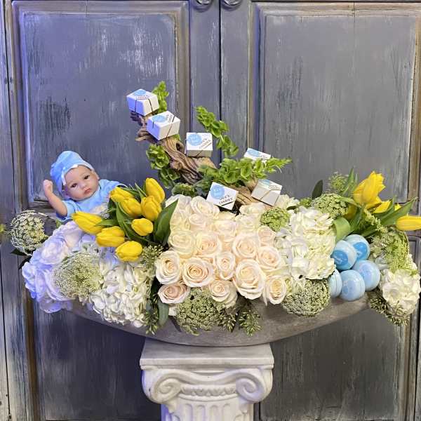 Floral arrangement with yellow tulips, pale roses, and a baby doll.