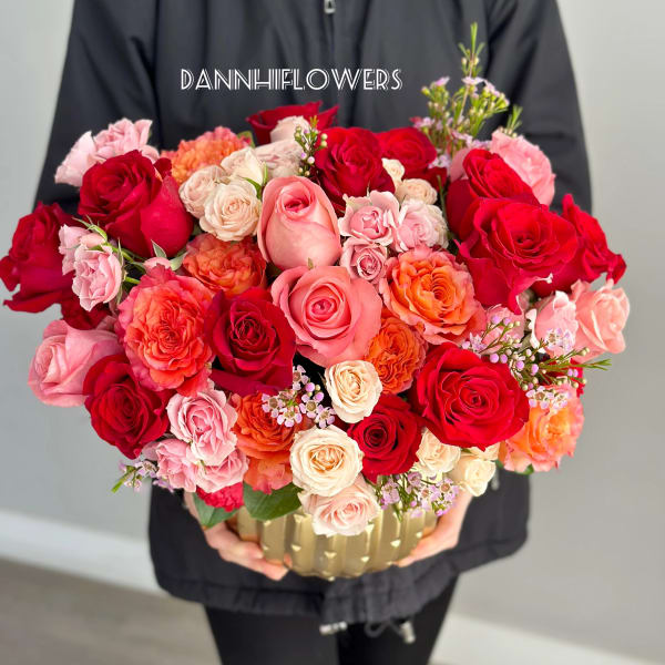 Large bouquet of red, pink, and peach roses in a gold container