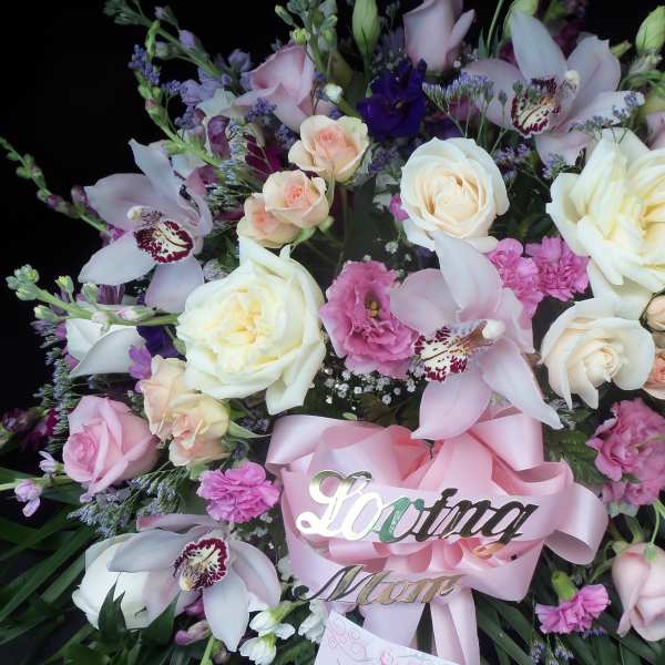Pink and white floral spray with roses and orchids, accented by a pink ribbon
