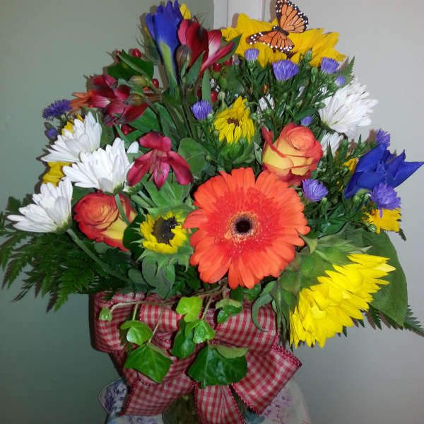 Mixed bouquet with gerbera daisies, roses, and a butterfly decoration in a vase