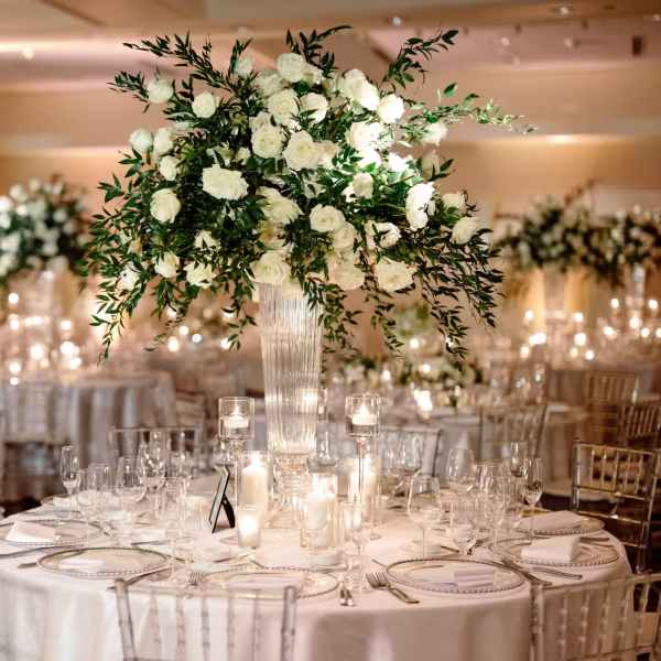 White rose centerpiece in a tall glass vase on a candlelit banquet table