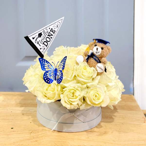 Cream rose arrangement in a round box with a teddy bear and graduation flag