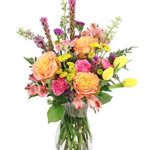 Mixed bouquet of peach roses, pink flowers, and yellow tulips in a glass vase