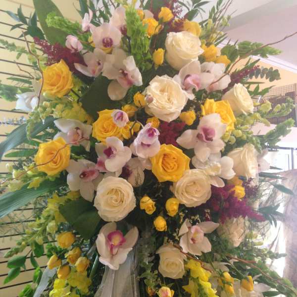 Large standing floral arrangement with yellow and white roses and orchids