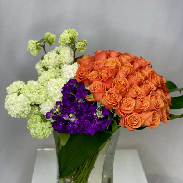 Orange roses and purple flowers in a clear glass vase with pale green blooms