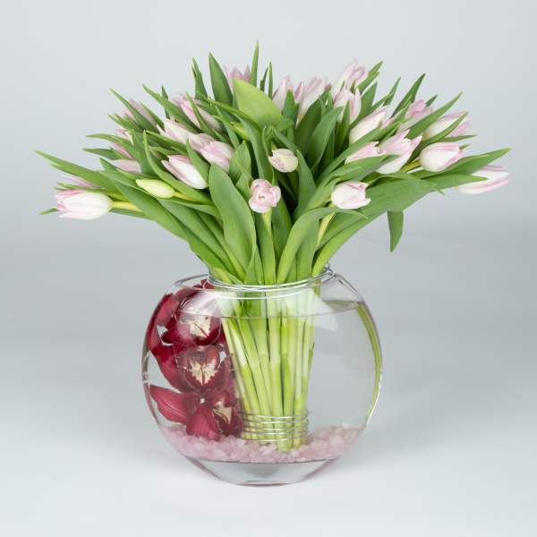 Pink tulips in a round glass vase with red orchids inside