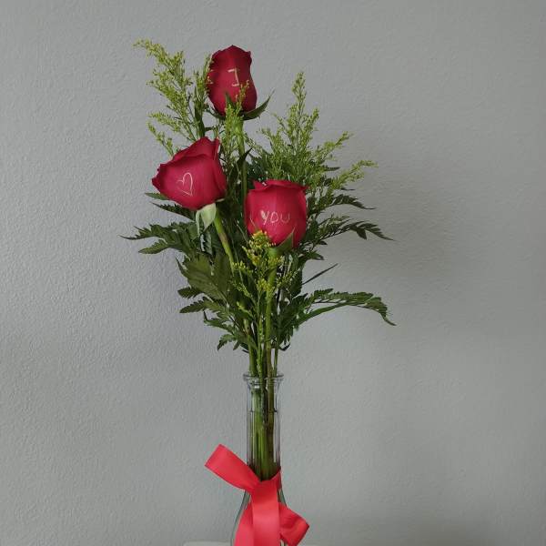 Three red roses in a clear glass vase with a pink ribbon