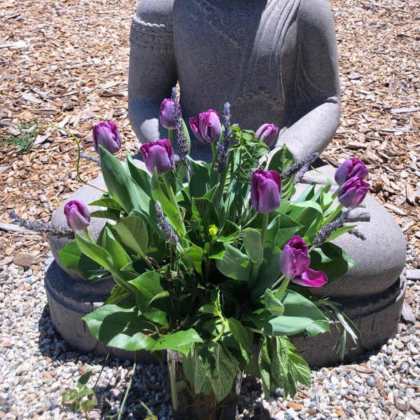 Purple tulips arranged in a glass vase in front of a stone statue