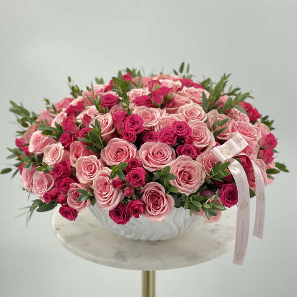 Round bouquet of pink and hot pink roses in a white bowl vase