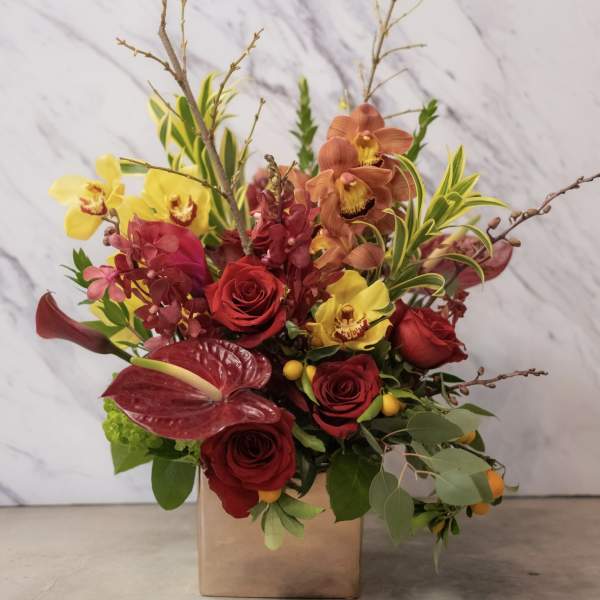 Mixed bouquet of red roses, yellow orchids, and burgundy anthurium in a square vase