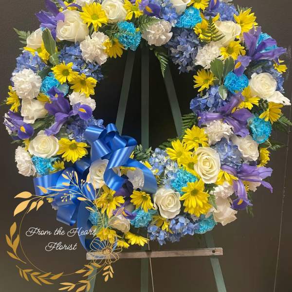 Circular floral wreath with white roses, blue hydrangeas, yellow daisies, and purple irises