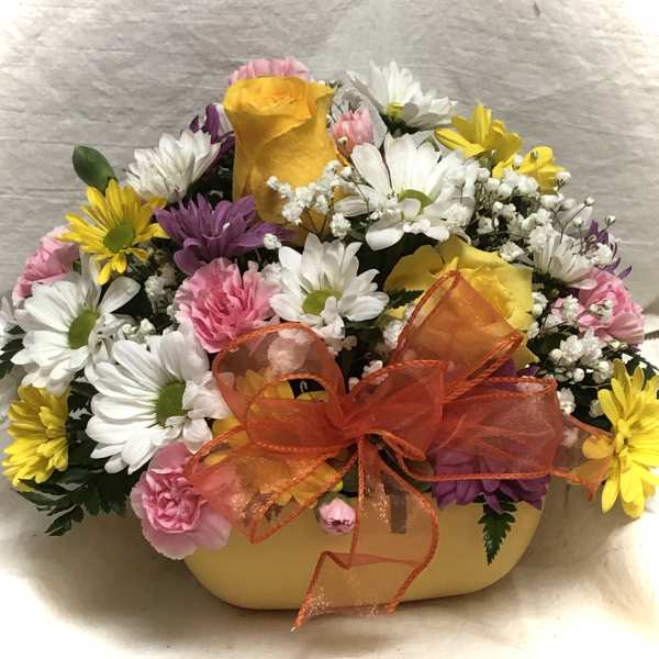Mixed bouquet of daisies, roses, and carnations in a yellow container with an orange bow