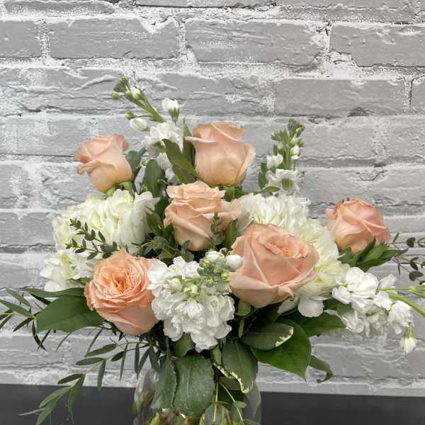 Peach roses and white flowers arranged in a clear glass vase