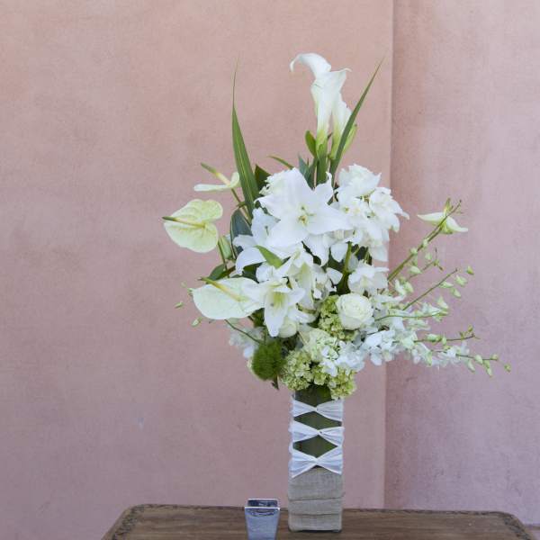 Tall white floral arrangement in a wrapped vase against a pink wall