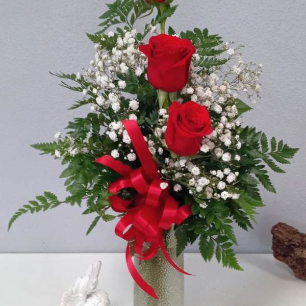 Three red roses in a glass vase with baby's breath and a red ribbon