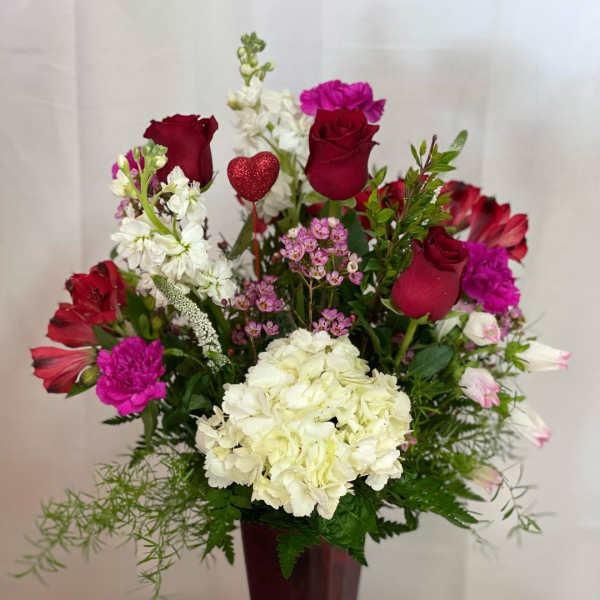 Mixed bouquet of red roses, white hydrangea, and pink flowers in a tall vase