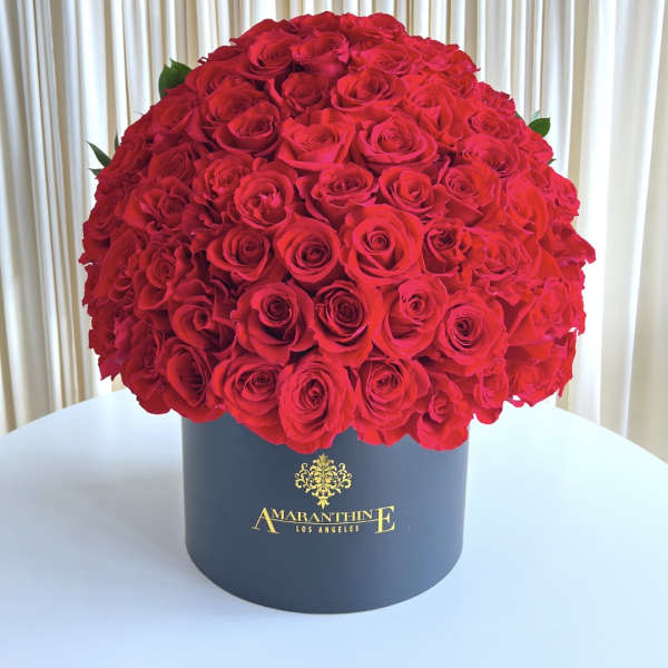 Large dome of red roses arranged in a black hatbox on a white table