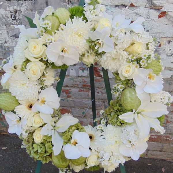 Standing wreath of white roses, orchids, lilies, and mums on a green easel.