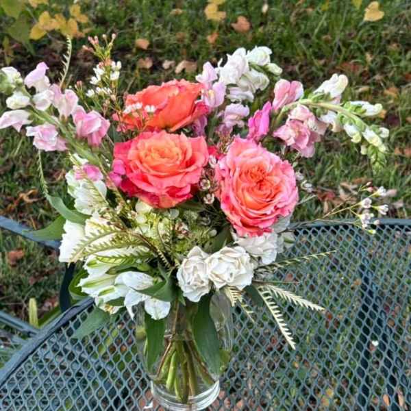 Pink and coral roses in a clear glass vase with white accent flowers
