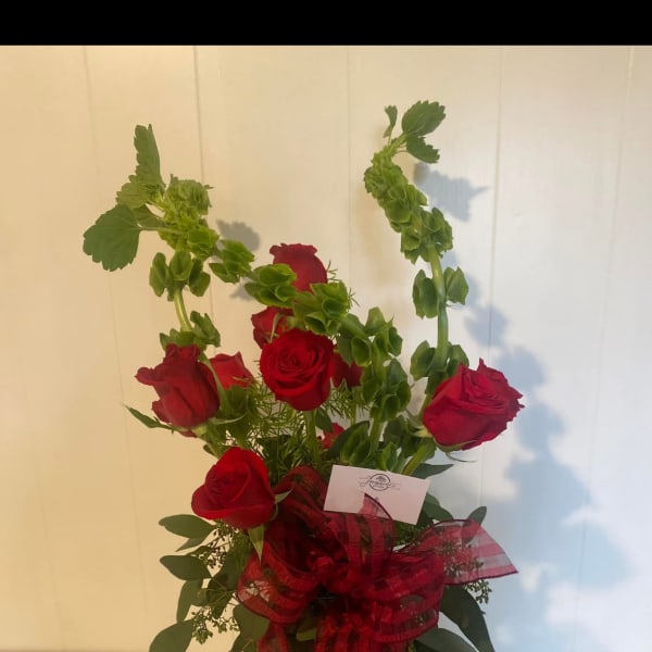 Red roses arranged in a glass vase with a red ribbon