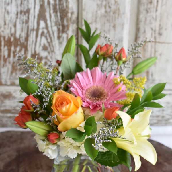 Mixed bouquet with roses, a pink gerbera daisy, lilies, and a glass vase