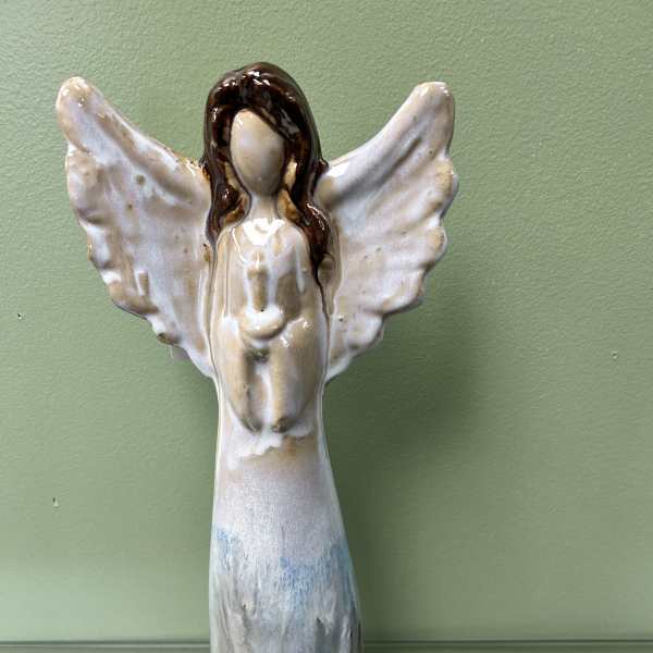 Ceramic angel figurine with outstretched wings on a green wall