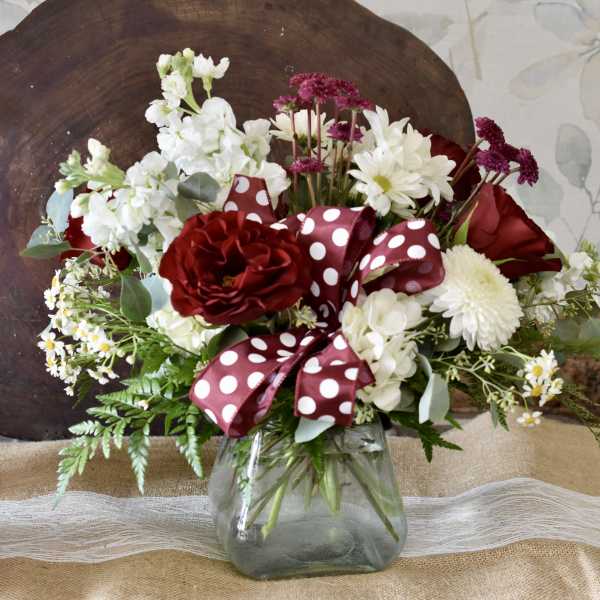 Red and white flower arrangement in a glass vase with a polka-dot ribbon