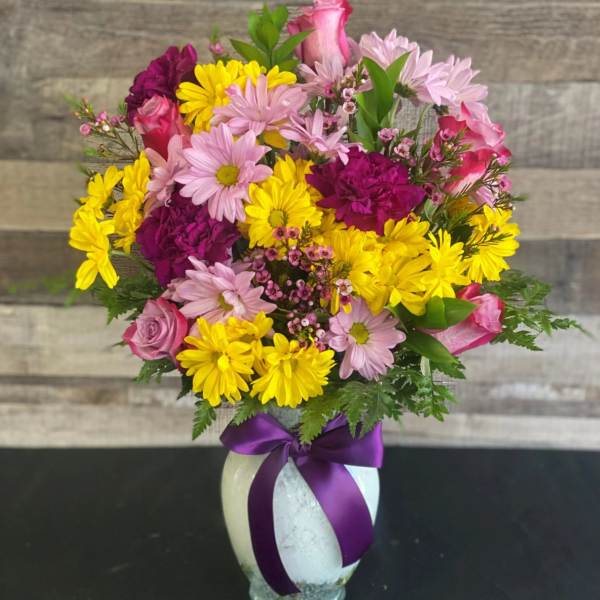 Mixed pink, yellow, and purple bouquet in a white vase with a purple ribbon