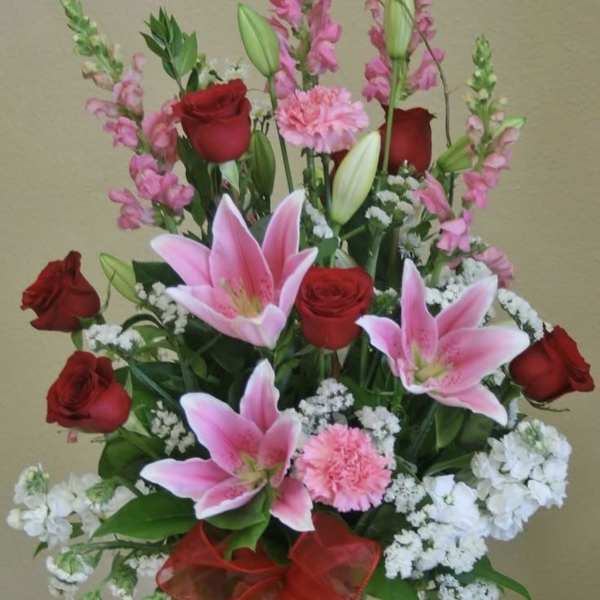 Bouquet of pink lilies and red roses in a glass vase with a red ribbon