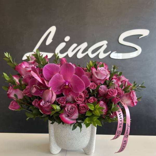 Pink orchid and rose arrangement in a gray vase with a ribbon