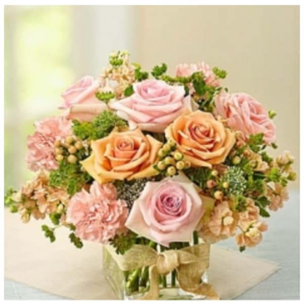 Pink and peach roses arranged in a clear glass vase with a ribbon