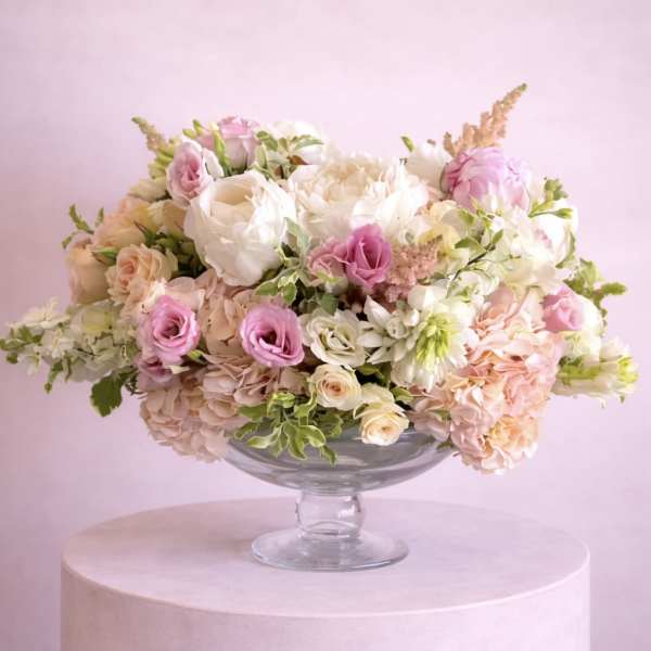 Pink and white floral arrangement in a clear glass compote vase