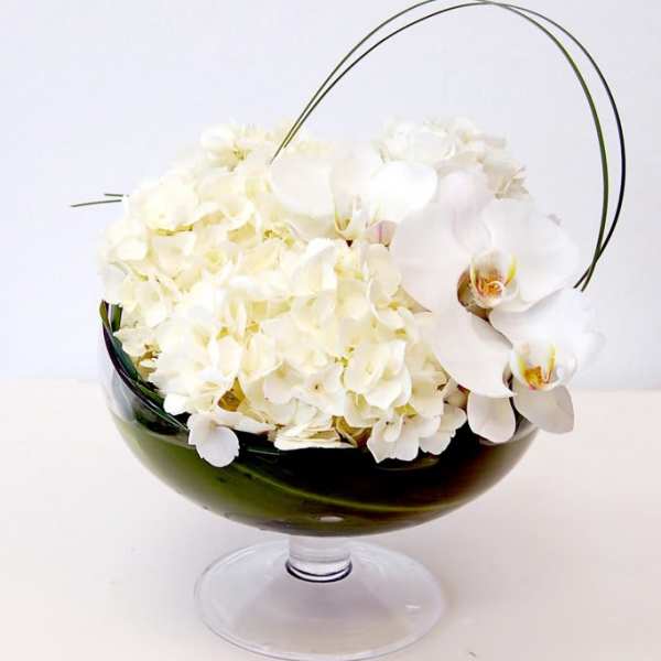 White flowers arranged in a dark glass pedestal bowl with arched handles