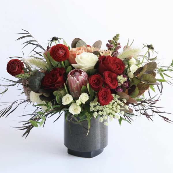 Arrangement of red and cream roses with protea and other blooms in a dark gray vase