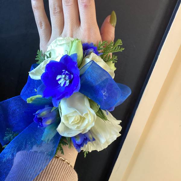 Hand corsage with white and blue flowers and a large blue ribbon