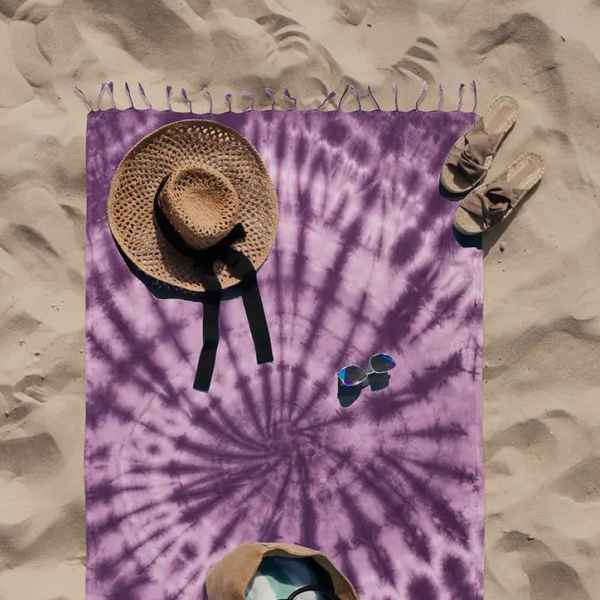Purple tie-dye beach blanket with a straw hat, sandals, sunglasses, and a tote bag
