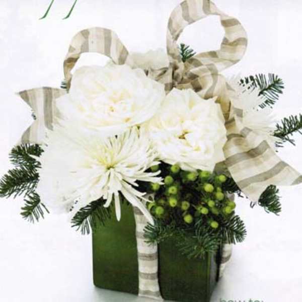 White flowers in a green box with striped ribbon and evergreen accents