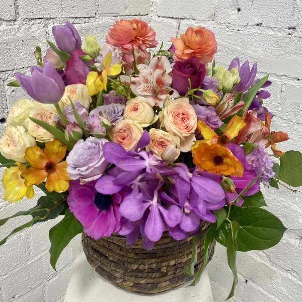 Mixed bouquet in a woven basket with purple, pink, orange, and yellow blooms