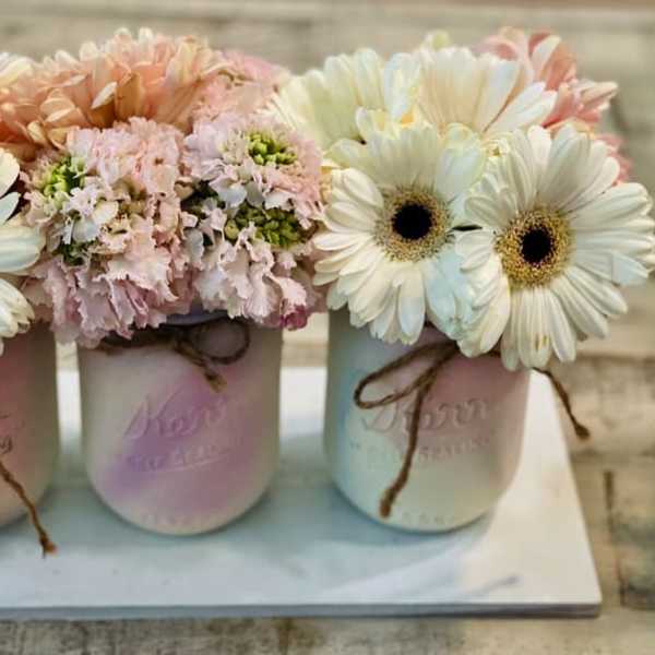 Three pastel mason jars with daisy and pink flower arrangements