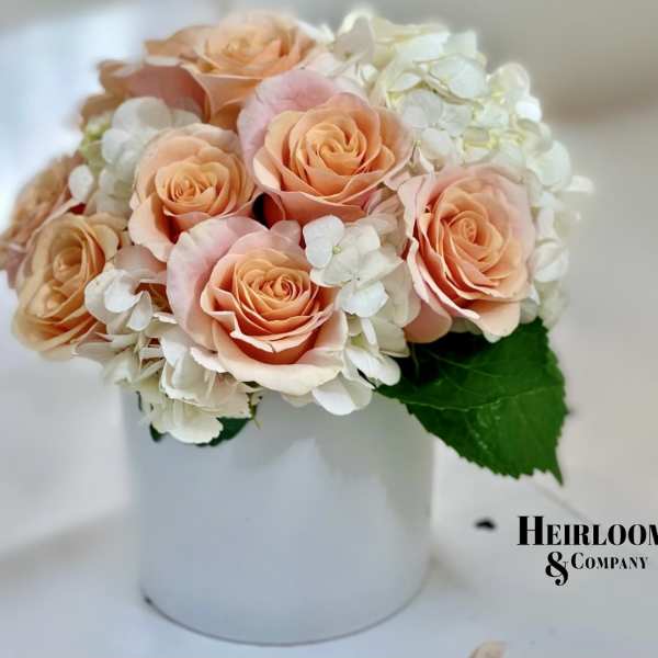 Peach roses and white hydrangeas in a white hatbox
