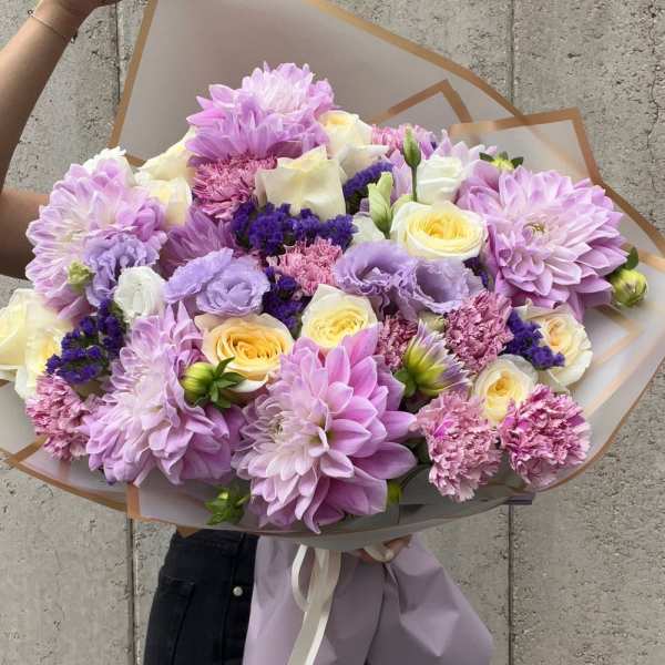 Large bouquet of lavender, cream, and yellow flowers wrapped in paper