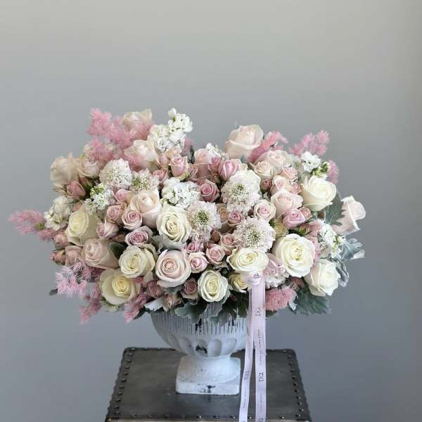 Large pastel bouquet of roses and white filler flowers in a white urn vase