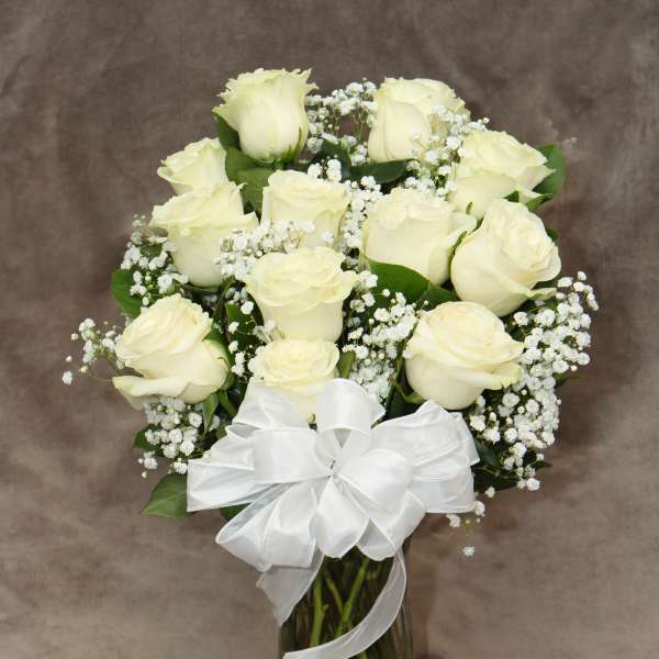 White roses arranged in a glass vase with baby's breath and a white ribbon
